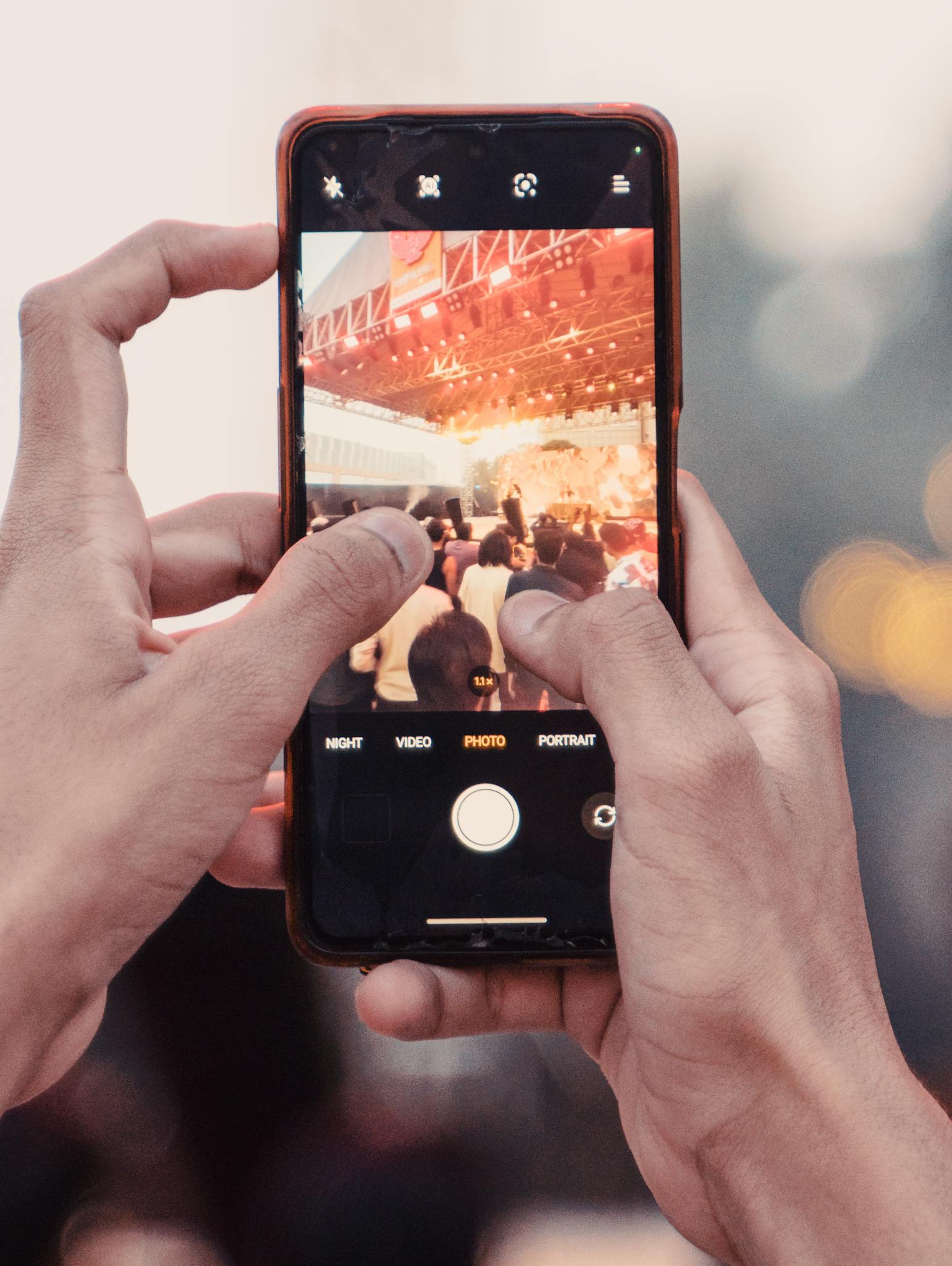 A close-up shot of hands holding a phone capturing a live music concert.