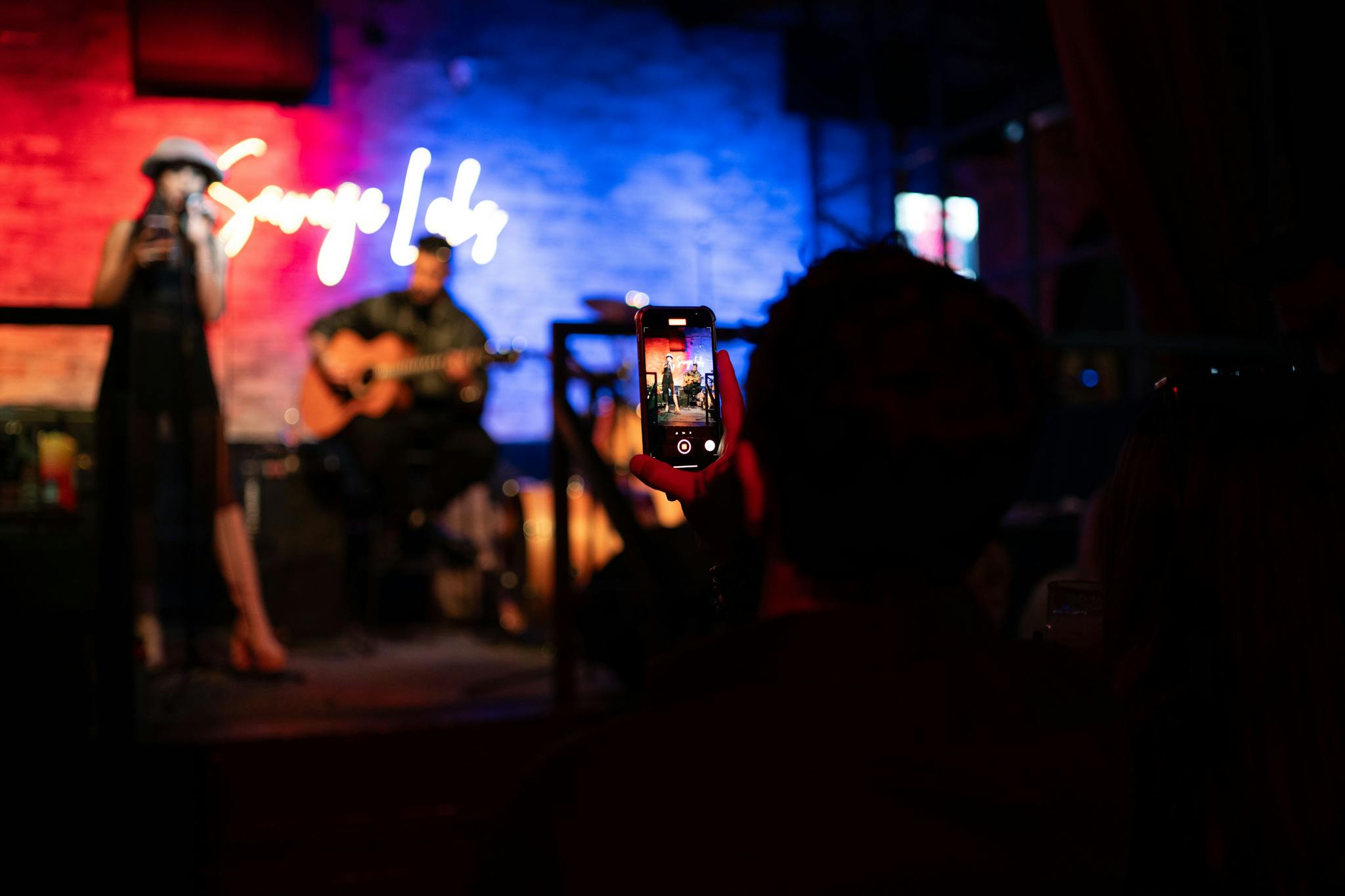 A live music performance captured with a smartphone, showcasing a singer and guitarist on stage.